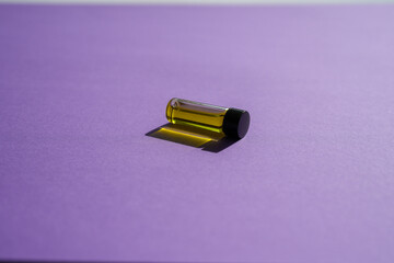 Small bottle of essential oil on its side on purple background