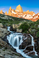 Fitz Roy Mountain in the background with a beautiful waterfall in the foreground during sunrise,...