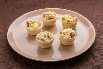 Salad in tartlets on a beige plate on a brown tablecloth
