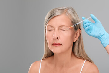 Doctor giving facial injection to senior woman on light grey background, closeup and space for...