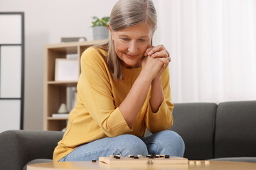 Obraz premium Thoughtful senior woman playing checkers at home