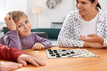 Family playing checkers at wooden table in room