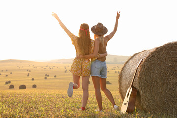 Hippie women near hay bale in field, back view - obrazy, fototapety, plakaty