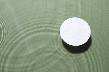 Cotton pad in micellar water on olive background, top view. Space for text