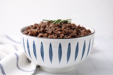 Fried ground meat in bowl and rosemary on white tiled table, closeup