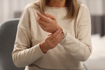 Mature woman suffering from pain in hand indoors, closeup. Rheumatism symptom