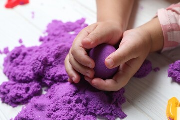 Little child playing with kinetic sand at white table, closeup