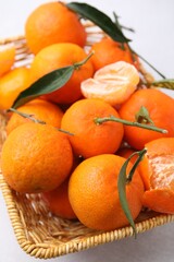 Fresh ripe tangerines with green leaves in wicker basket on white table, closeup