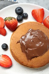 Tasty pancakes with chocolate paste and berries on plate, top view