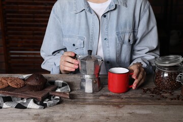Fototapeta na wymiar Brewing coffee. Woman with moka pot, cup, cookies and muffin at wooden table, closeup