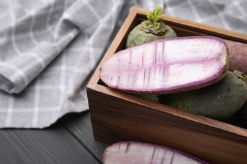 Purple and green daikon radishes in crate on black wooden table, closeup. Space for text