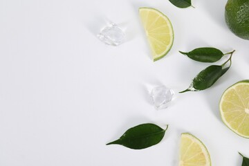Flat lay composition with fresh limes, leaves and ice cubes on white background. Space for text