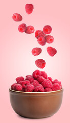 Fresh ripe raspberries falling into bowl on pink background