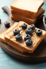 Delicious toasts with peanut butter and blueberries on light blue wooden table, closeup