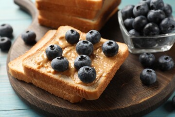 Delicious toasts with peanut butter and blueberries on light blue wooden table, closeup
