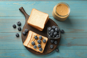 Delicious toasts with peanut butter and blueberries on light blue wooden table, top view