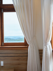 Old window with wooden frame and light curtain in traditional house style with beautiful view.