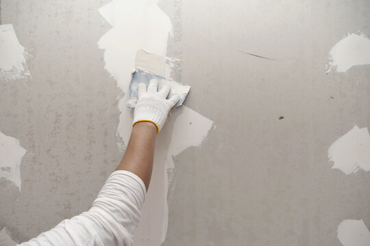 Plasterwork and wall painting preparation. close up hand of craftsman applying filling drywall patch.