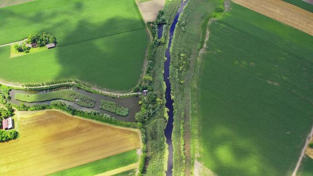 Aerial view of a plain countryside and a pond and river in a shadow of a cloud
