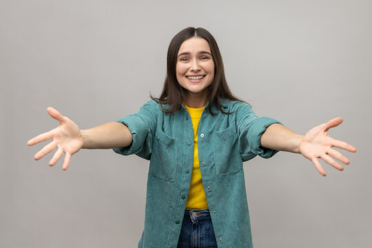 Come into my arms, free hugs. Portrait of adorable hospitable woman smiling and reaching out hands, going to embrace, wearing casual style jacket. Indoor studio shot isolated on gray background.