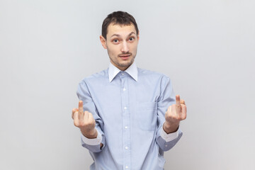 Portrait of impolite serious rude man standing looking at camera and showing middle fingers, arguing with somebody, wearing light blue shirt. Indoor studio shot isolated on gray background.