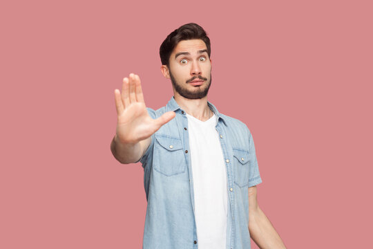 Slow down. Displeased bearded man shows stop gesture, asks to hold horses, keeps palms towards camera, says take it easy and control your behavior. Indoor studio shot isolated on pink background.