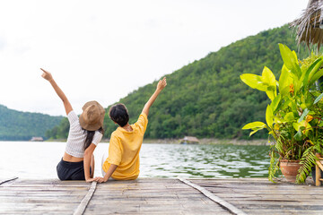 Happy Asian lesbian couple enjoy and fun outdoor lifestyle travel nature forest mountain on summer holiday vacation. LGBTQ person relaxing together on lake house balcony with looking beautiful nature. - obrazy, fototapety, plakaty