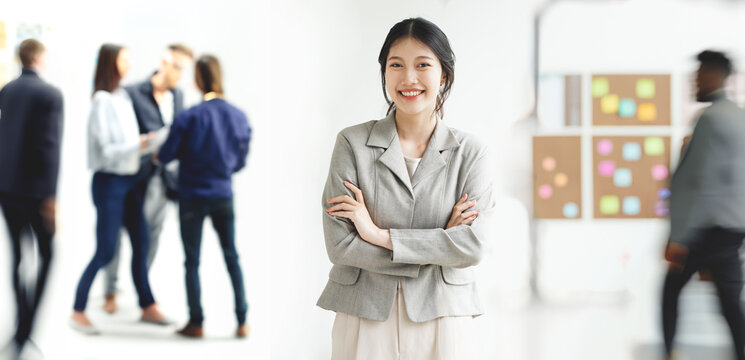 Portrait of young white woman with arms crossed stanging in a busy modern workplace