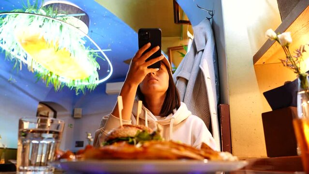 Young woman take photo of burger plate in front in vegetarian restaurant