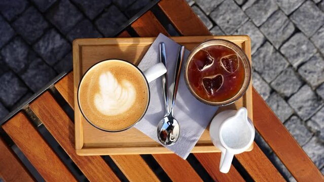 Top down view of ice coffee and latte cups with spoons on wooden outdoor table