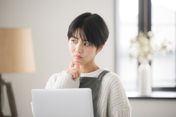 A woman who looks like a sales clerk or customer service worker in a store, using a computer in her room and looking annoyed and distressed about sales, etc. close-up