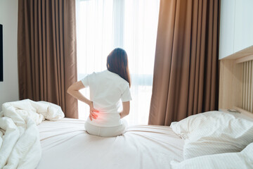 woman having back body ache during sitting on bed at home. adult female with muscle pain after...