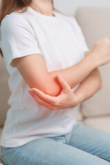 Woman having elbow ache during sitting on couch at home, muscle pain due to lateral epicondylitis or tennis elbow. injury, Health and medical concept