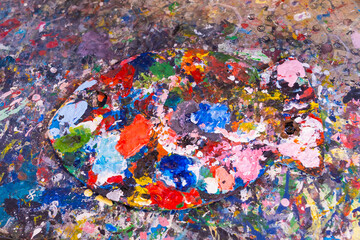 From above rough palette with stains of dry multicolored paint placed on table in studio. Colorful painting palette, Macro close up acrylic background. Modern art concept.