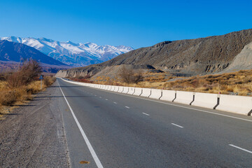 empty highway road with separating concrete barrier in mountains at sunny autumn day.