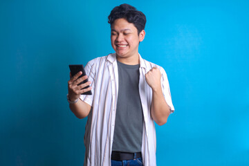 Smiling happy Asian man using smartphone while clenching fist celebrating victory