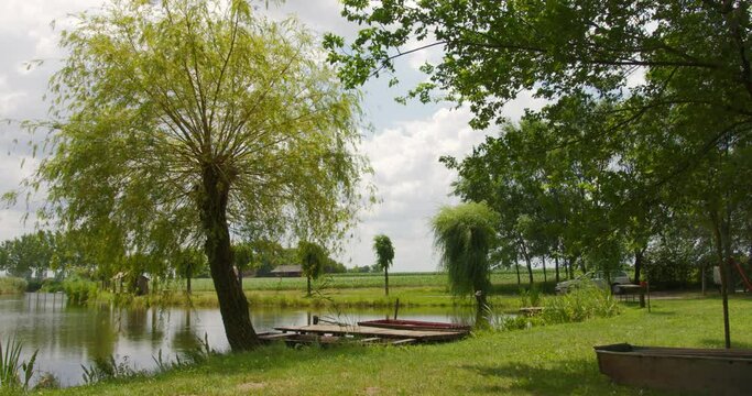 Idyllic footage of small wooden pier and boats on a green shore of a pond