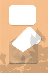 Natural light casts shadows from the leaves of a tree branch an envelope with two sheets of white paper on orange background. Mock up Vertical orientation