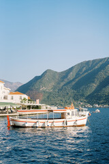 Fototapeta na wymiar Tourist boat is moored off the coast of Perast against the backdrop of mountains. Montenegro