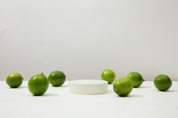 Plump green lemons stand out on a white background with a round platform placed in the center of the frame. Lemon is an effective skin beautifying food, treating acne and dark scars.