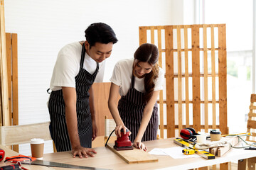 Workshop Learning: A Carpenter Guides a Woman in Using an Electric Sander for Woodwork Projects