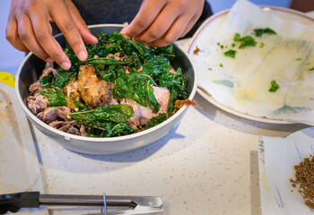 Hands spread fried mint over a leg of roast lamb on the kitchen benchtop. Home cooking and...