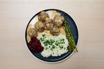 A plate of Swedish meatballs with asparagus, mash potato, and lingonberry.