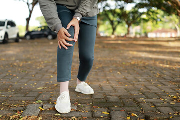 Fototapeta premium Joint pain, Arthritis and tendon problems. an asian muslim woman touching knee at pain point in the park. Close up photo