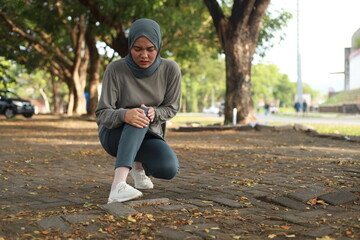 Joint pain, Arthritis and tendon problems. an asian muslim woman touching knee at pain point in the park - obrazy, fototapety, plakaty