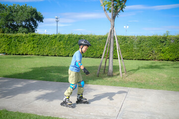 Cute little smiling Asian 7 years old child rollerblading in protection, helmet in sunny summer...