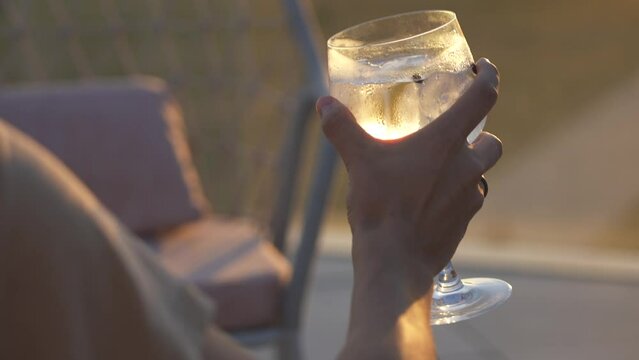 Man drinking a gin tonic. Savoring a cocktail on a terrace at golden hour, a guy enjoys the warm glow, blending relaxation and style in the tranquil evening ambiance. Summer vibes. Golden hour gin.