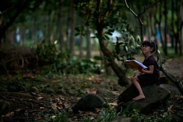 Naklejka na ściany i meble Little Child reading a book in a green coastal forest