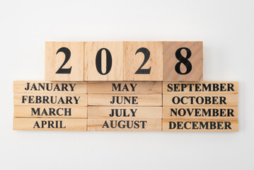 Year 2028 written on wooden cubes on top of the months of the year written on twelve rectangular pieces of wood. Isolated on white background - obrazy, fototapety, plakaty