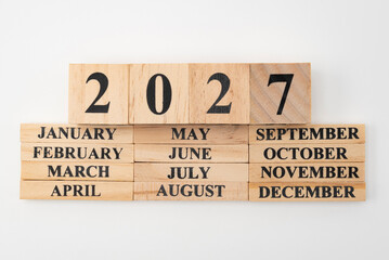 Year 2027 written on wooden cubes on top of the months of the year written on twelve rectangular pieces of wood. Isolated on white background